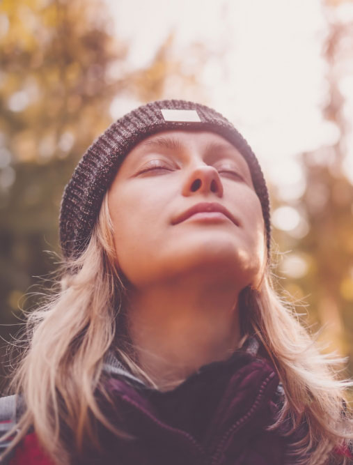 Woman wearing a black beanie lifting head to take a deep breath with eyes closed